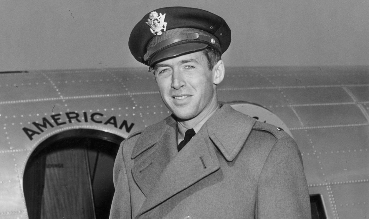 Portrait of American actor Jimmy Stewart (1908 - 1997) in his Air Force cap and wool overcoat, in front of a military airplane.