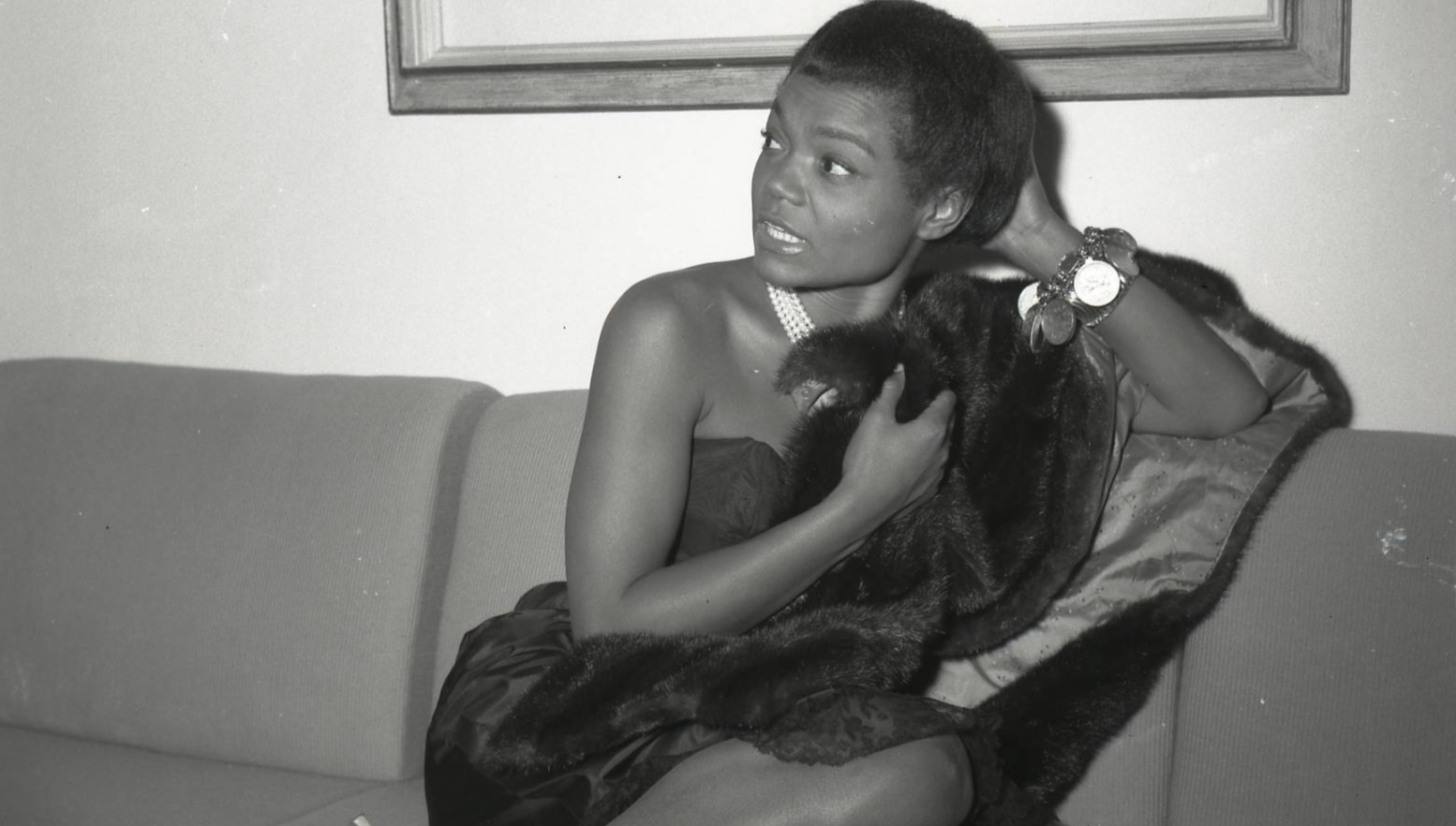Photo of Eartha Kitt sitting on a couch wearing black dress
