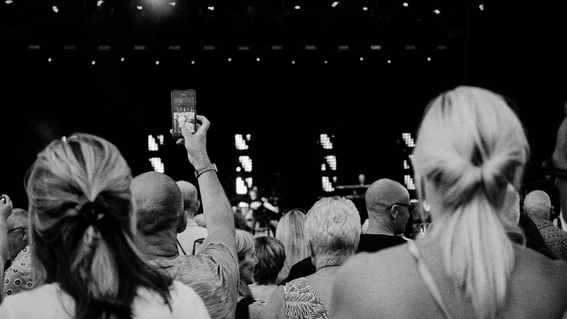 Black and white photo of a concert audience capturing memories with a smartphone.