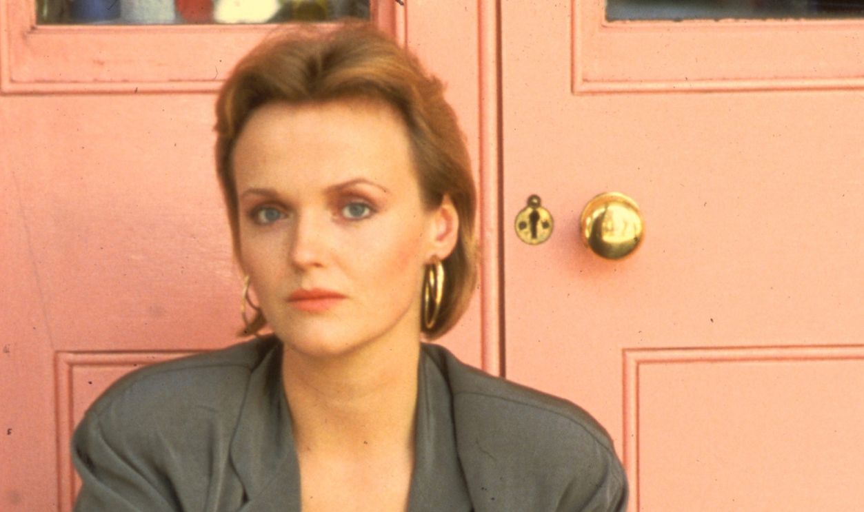 Actress Miranda Richardson is shown seated on a step outside of a building.