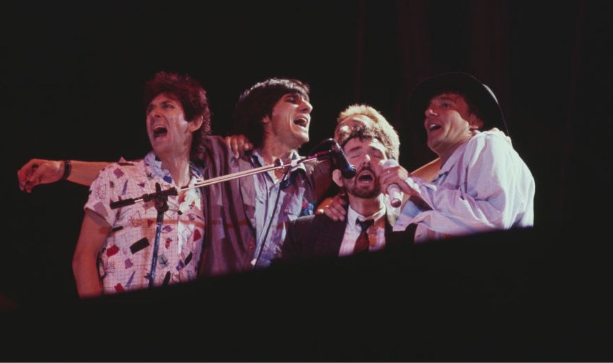British singer Rod Stewart (far right) performs live on stage with, from left, Ian McLagan, Ronnie Wood, Kenney Jones and Ronnie Lane (1946-1997) at a Faces reunion during the encore of a Rod Stewart show at Wembley Stadium in London in July 1986.