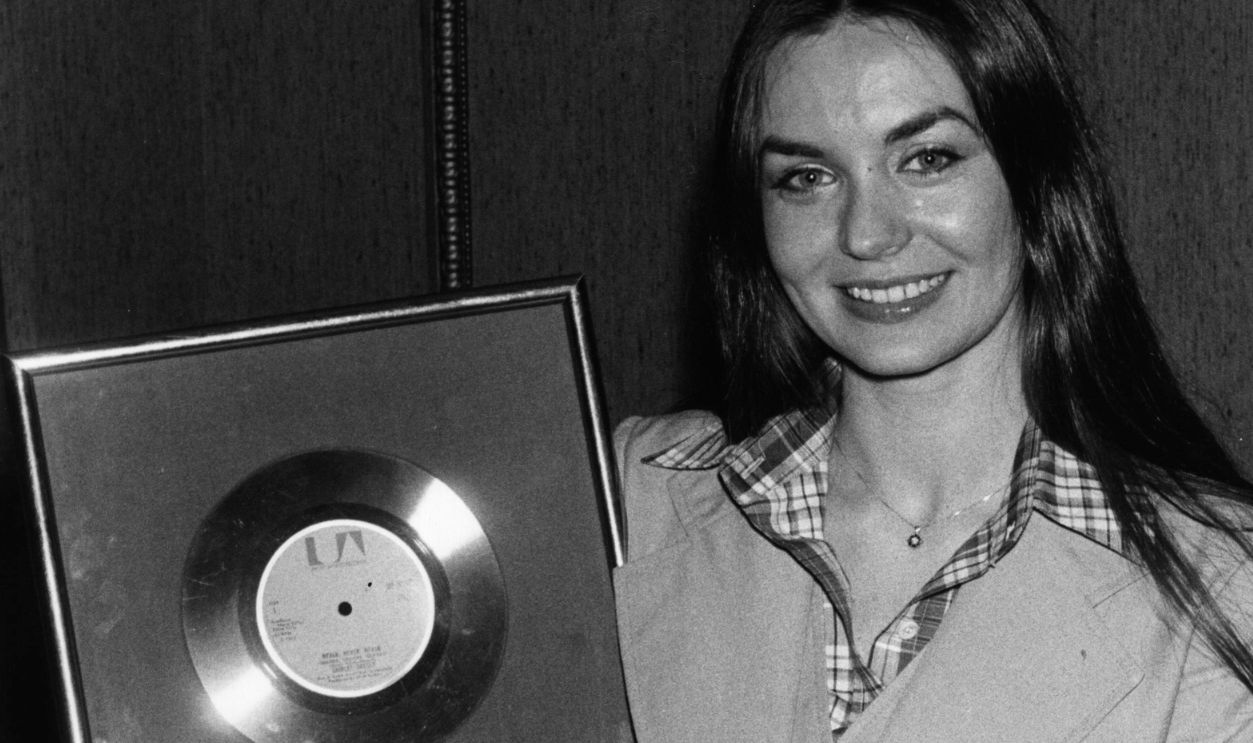 7th November 1977: American singer Crystal Gayle with a gold disc for 500,000 sales of her Grammy award winning hit single 'Don't It Make My Brown Eyes Blue'. Gayle's LP 'We Must Believe In Magic' was the first album by a female country star to sell in excess of 1,000,000 copies.