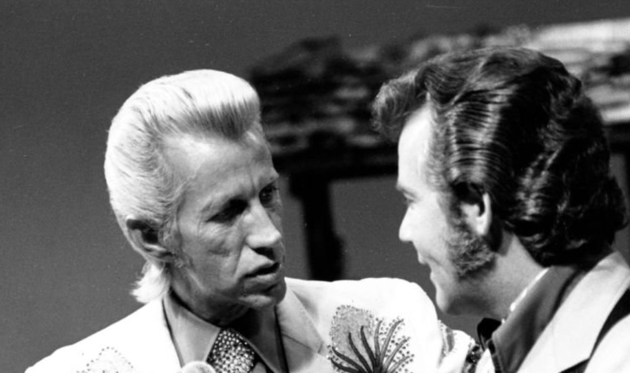 CIRCA 1975: Country singer Porter Wagoner interacts with a man holding an acoustic guitar in circa 1970. Mr. Wagoner is wearing a Nudie Suit designed by Nudie Cohn of Nudie's Rodeo Tailors.