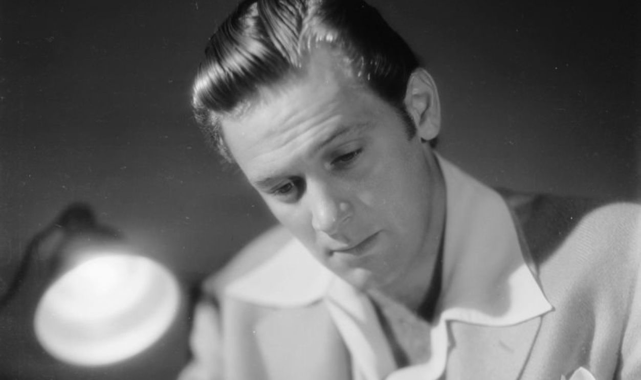 1939: American actor William Holden (1918 - 1981) reading a book by the light of a lamp. 