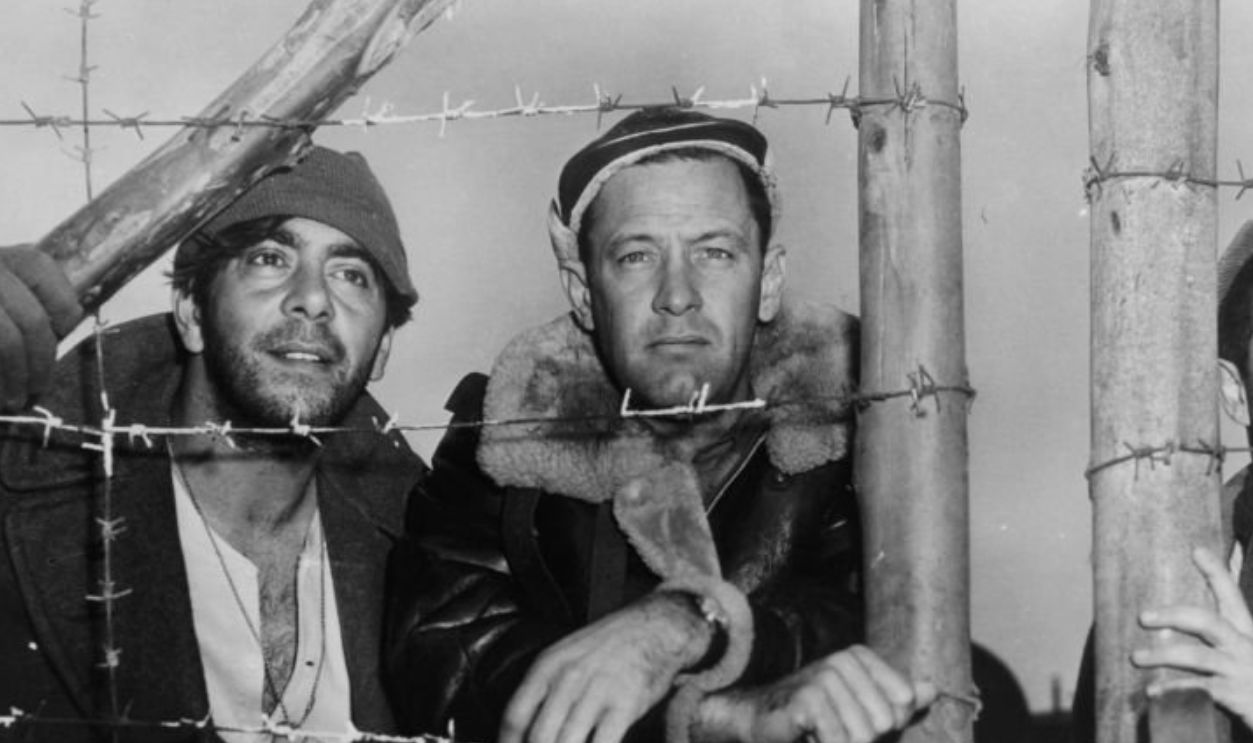 Robert Strauss, William Holden, and man looking through barbwired fence in a scene from the film 'Stalag 17', 1953. 