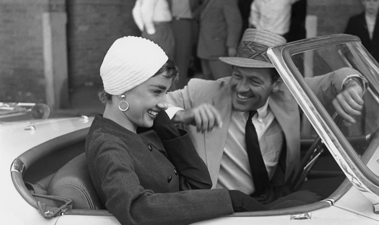 Actors Audrey Hepburn (1929 - 1993) and William Holden (1918 - 1981) in a Nash-Healey roadster on the set of director Billy Wilder's film, 'Sabrina' (aka 'Sabrina Fair'), New York, October 1953. Hepburn is wearing a skirt suit and hat designed by Hubert de Givenchy.