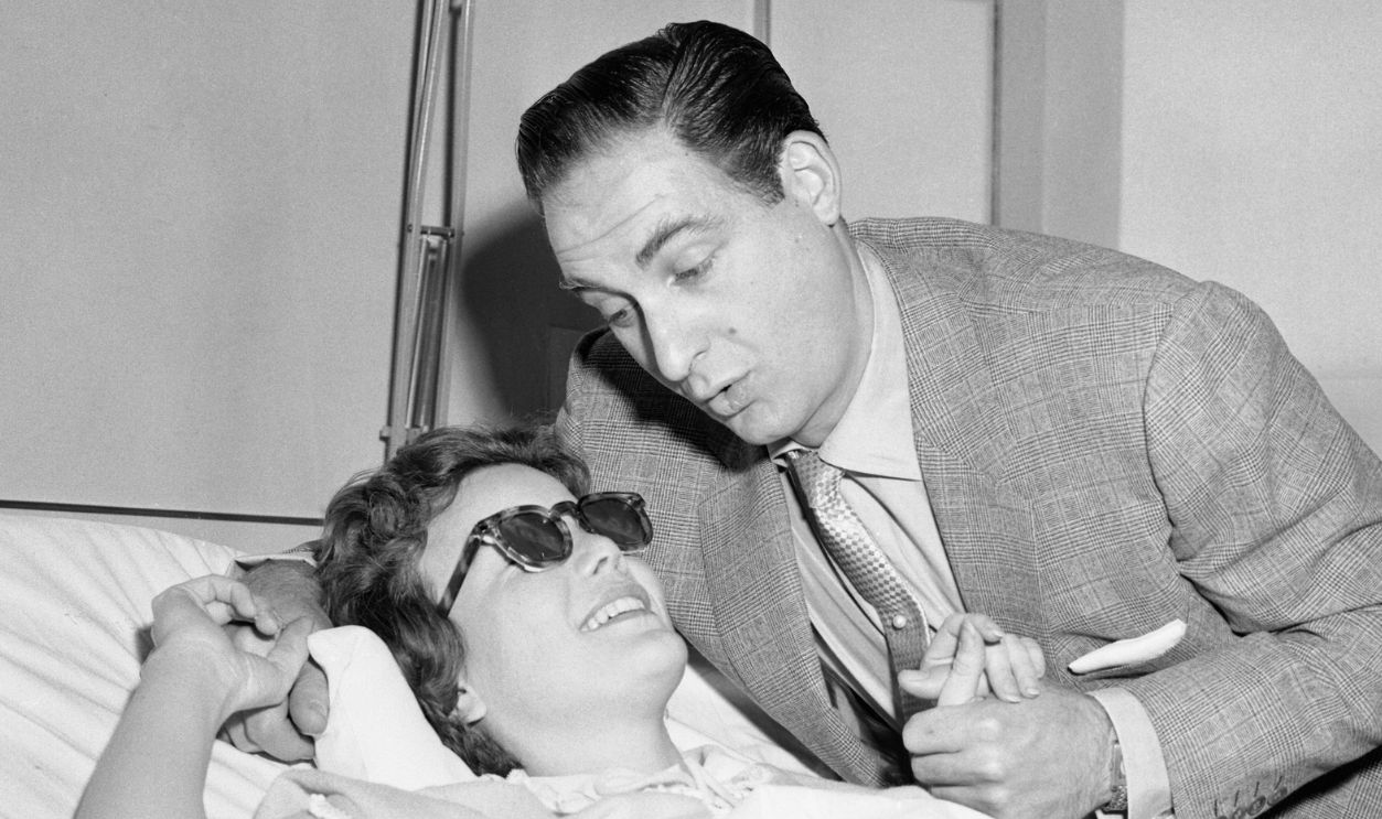 Television actress Nanette Fabray chats with her "TV husband" Sid Caesar, during his visit in her room at Mt. Sinai Hospital today. Nanette suffered a severe concussion last Monday night when a pipe fell on her head a few minutes before the show Caesar's Hour ended at the Century Theater. The pipe had been used to hold up the scenery. She'll be confined to the hospital for some time.