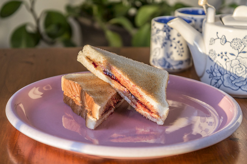 Close-up photo of Peanut butter and jelly sandwich in purple plate placed on a wooden table