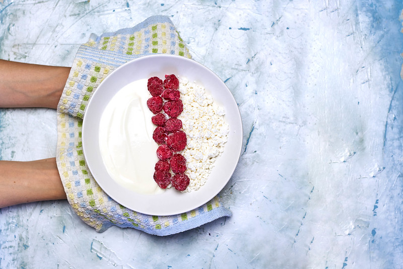 Woman holding a plate of healthy dieting meal cottage cheese and sour cream with raspberries