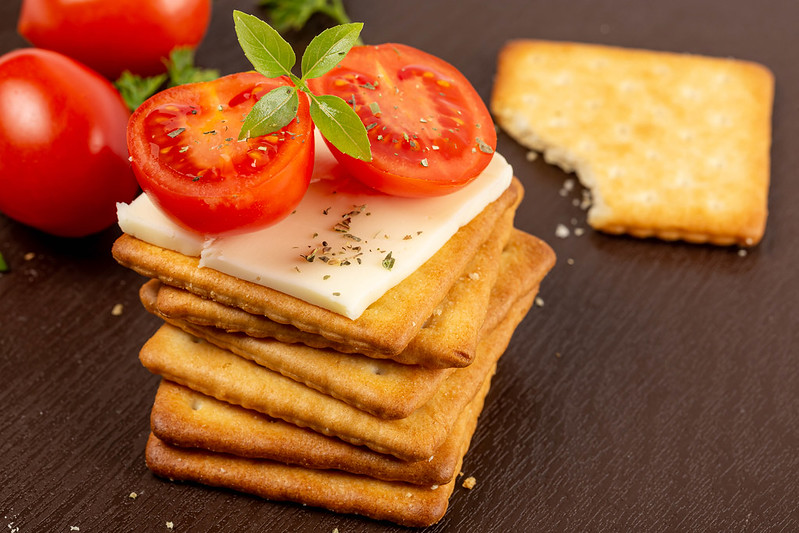 Stack of square crackers with slices of cheese, tomato and basil