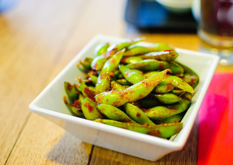 Close-up photo of edamame in a white bowl placed on a wooden table