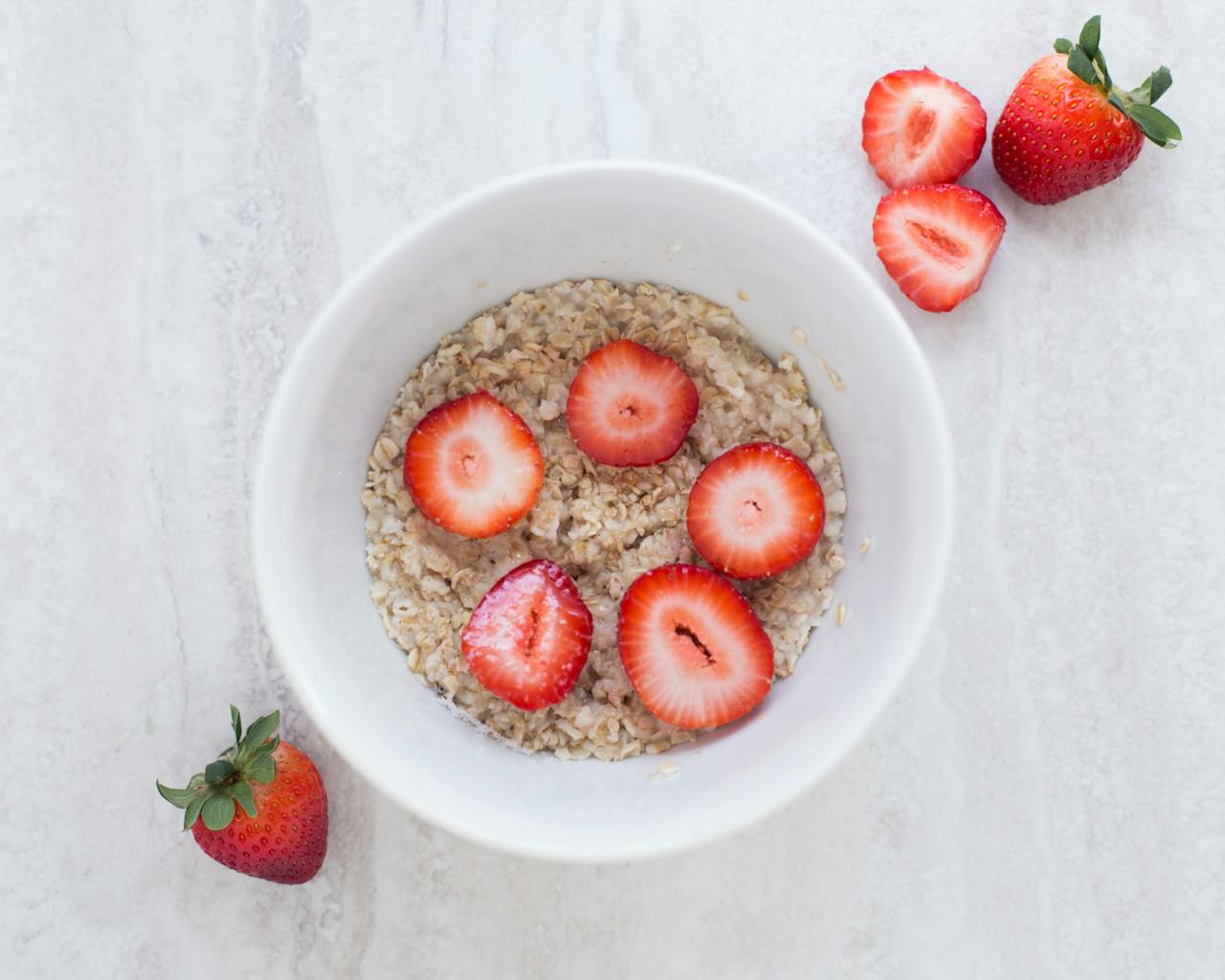 Strawberry on Table Top Near White Ceramic Bowl filled with oatmeal