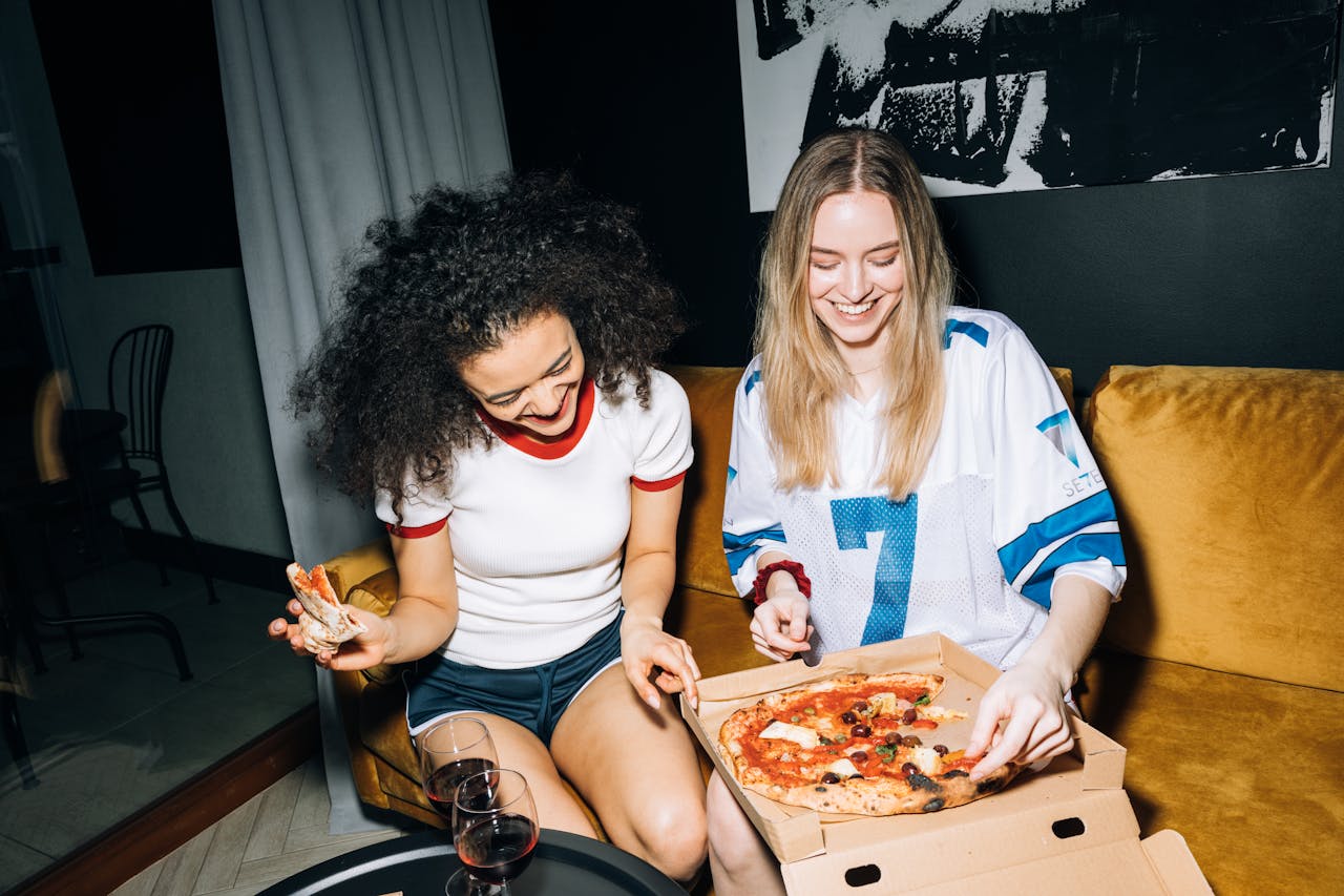 Two Young Women Eating and Getting a Slice of Pizza and smiling