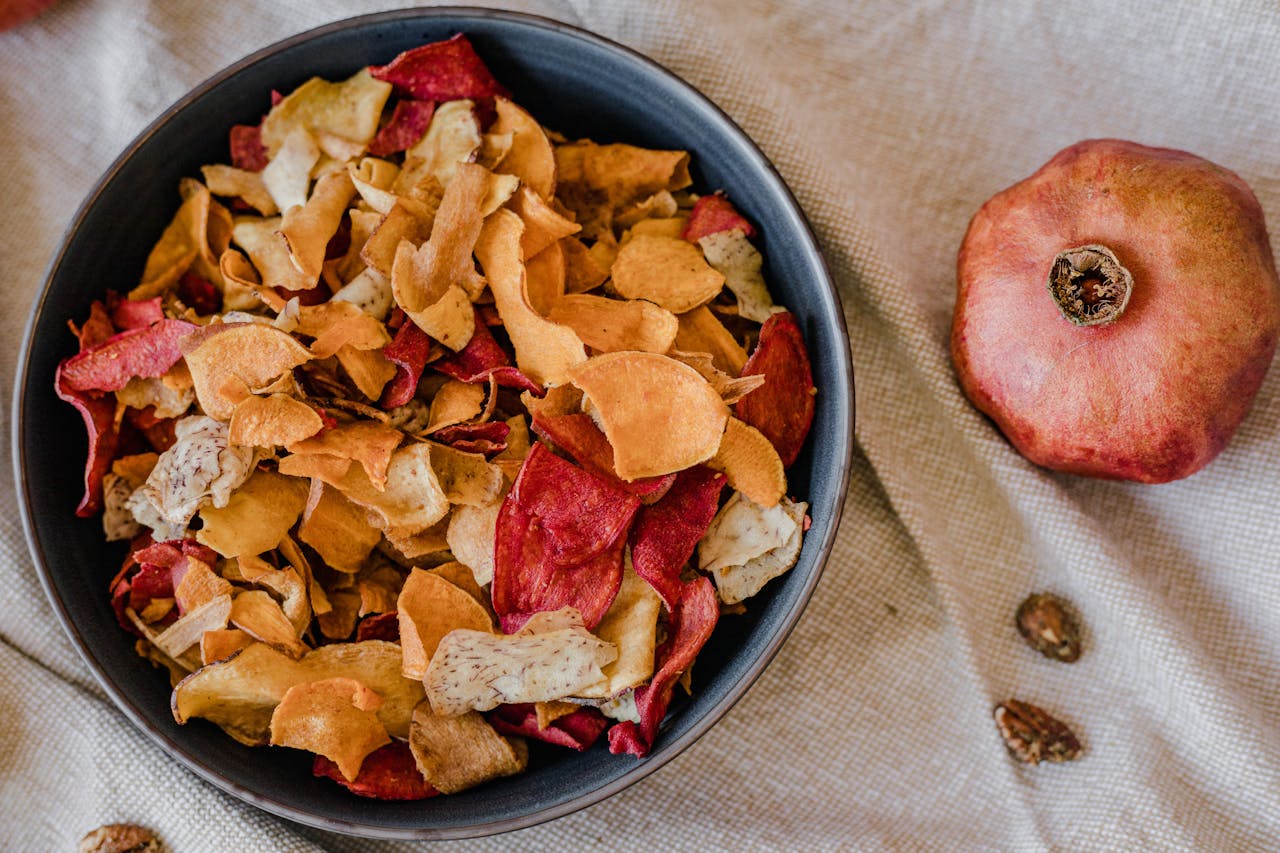 Close-up Photo of Vegie Chips in the Bowl next to a pomegranate