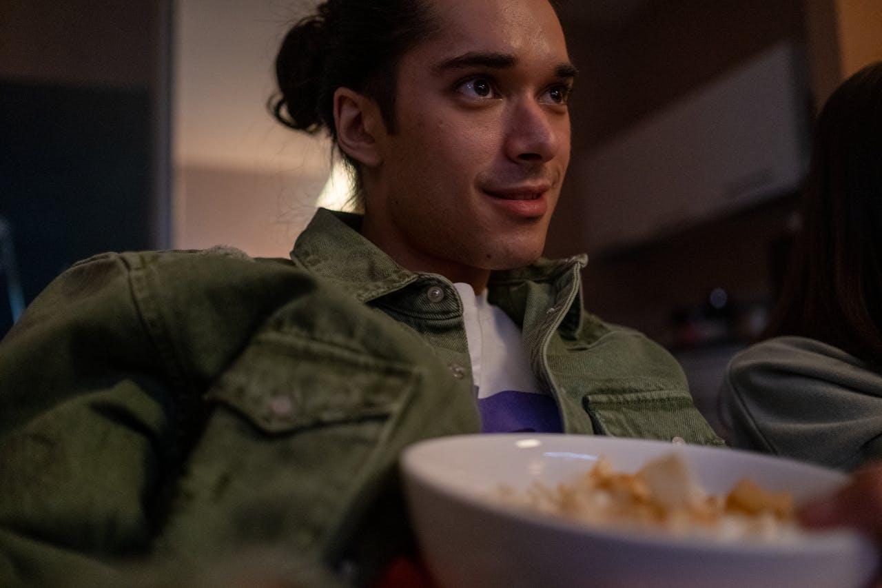 Young man eating snacks, watching TV and smiling