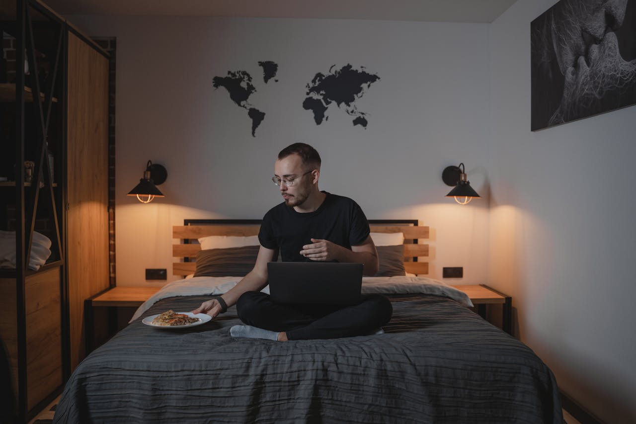 Man in Black Crew Neck T-shirt holding a plate with food and Using Black Laptop Computer