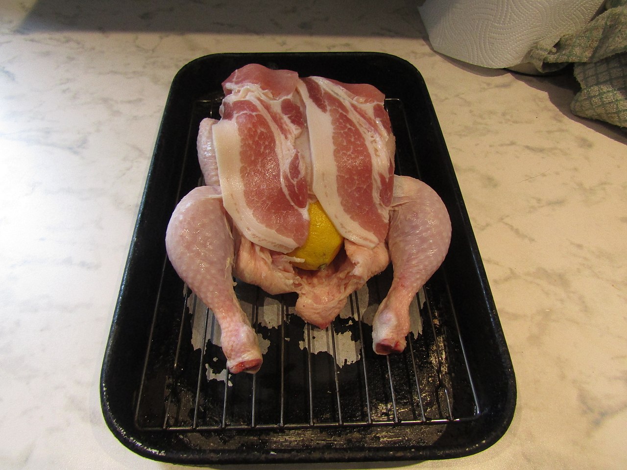 A chicken prepared with butter, lemon and bacon ready to be roasted in an oven