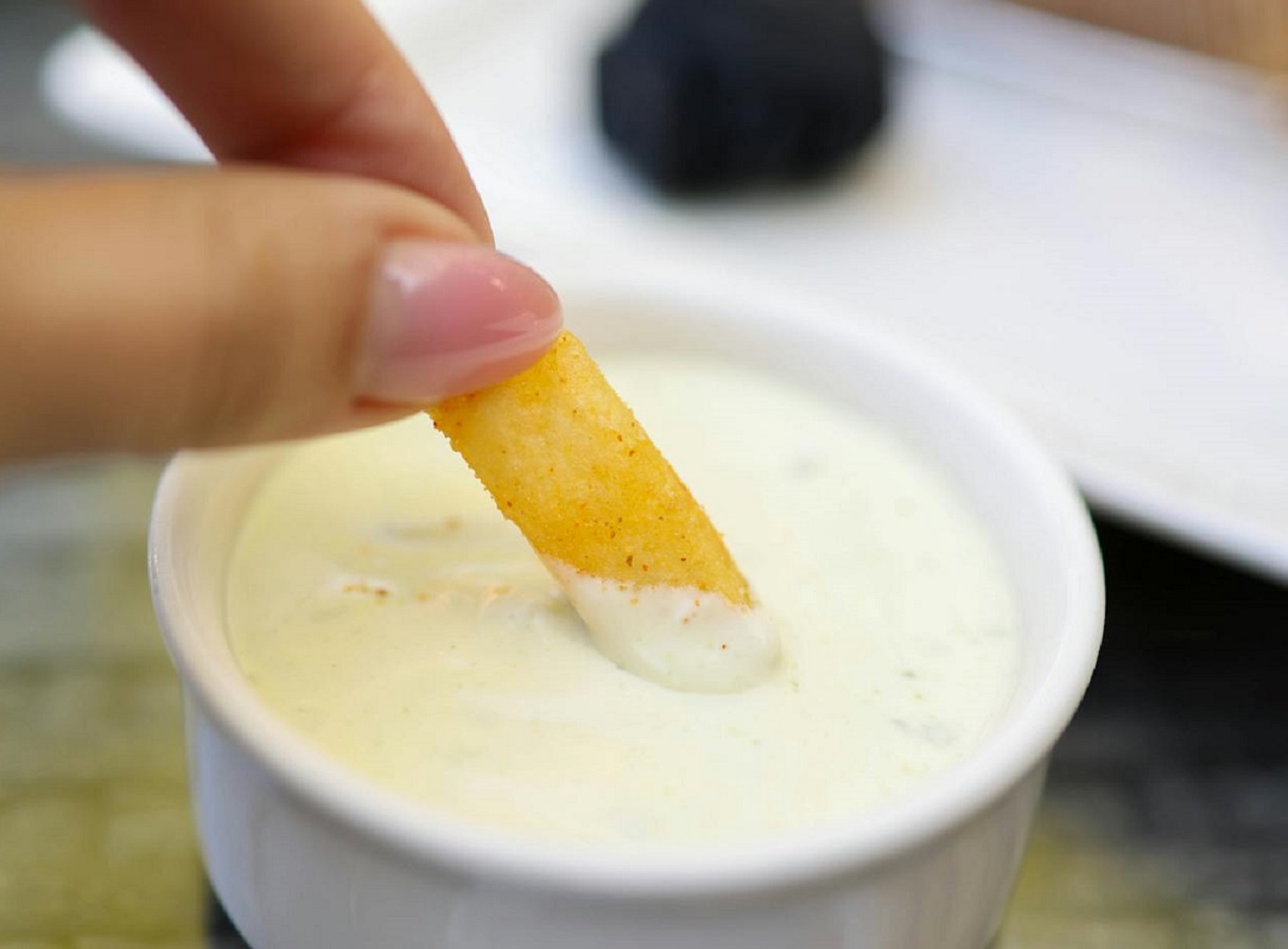 Fingers of a Woman Dipping in a White Dipping Sauce