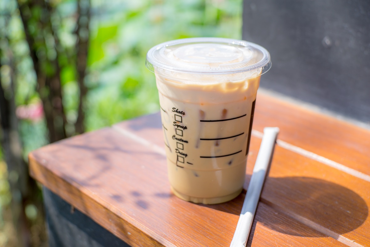 Frozen Capuchino in takeaway cup on wood and blur green background.