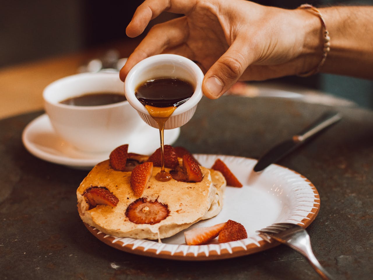 Pouring maple syrup on Pancakes with Strawberries