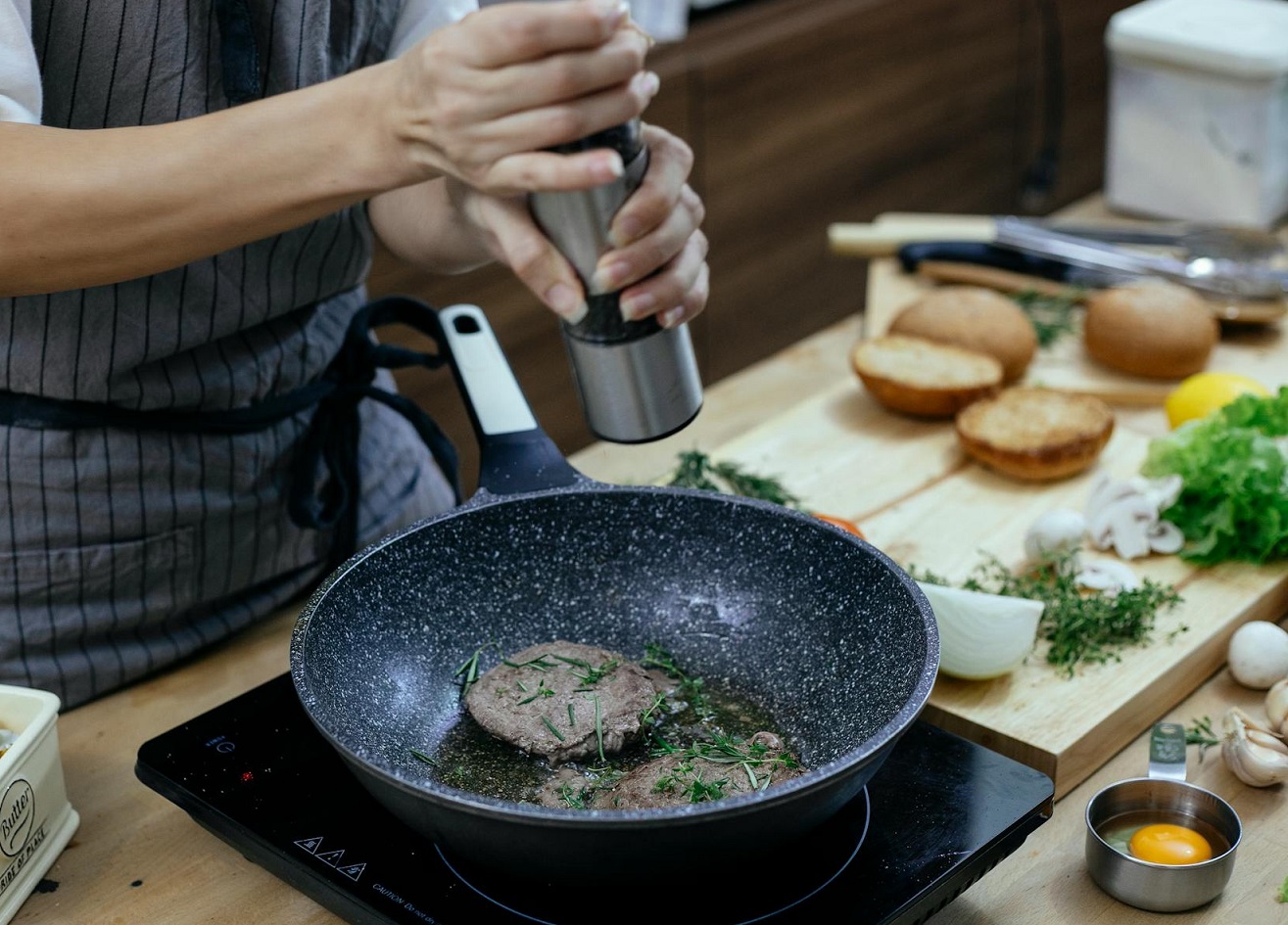 Woman adding spices in pan with meat.