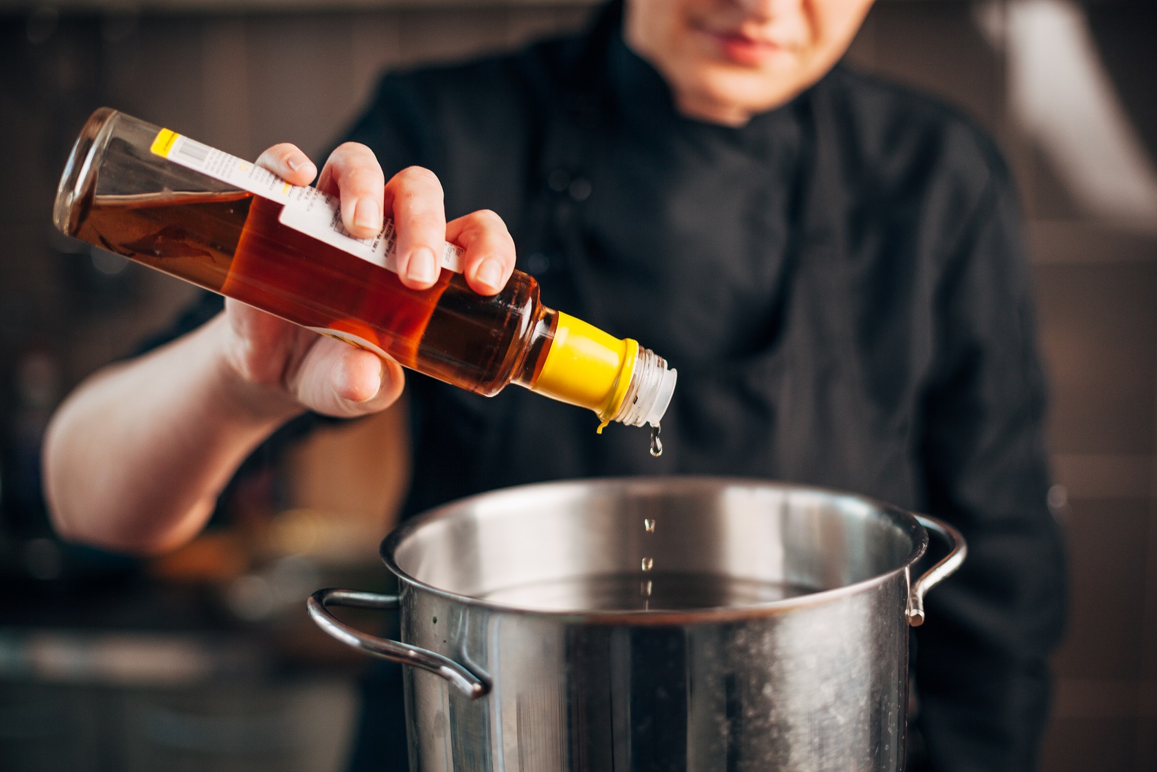 Female chef pouring vinegar in a pot with water.