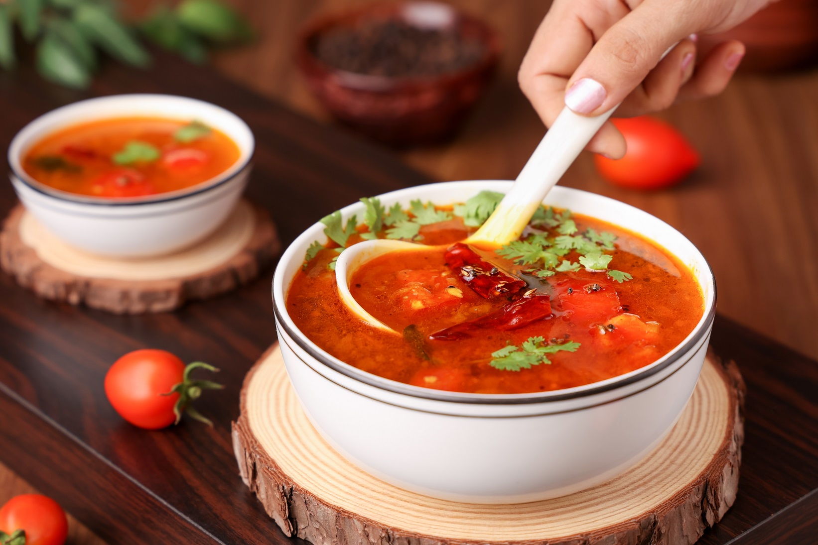 Woman hand serving tomato rasam curry hot spicy soup