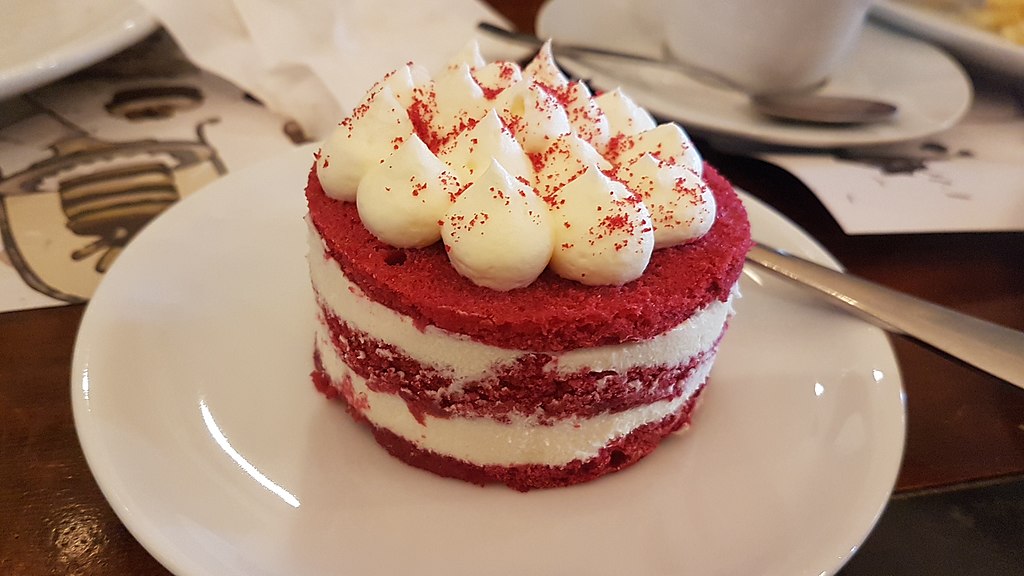 Close-up Photo of a Red velvet cake in a white plate next to metal fork
