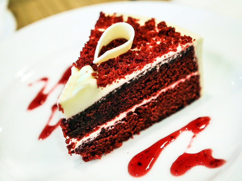 Close-up Photo of a Slice of Red Velvet Cake in a white plate placed on a wooden table