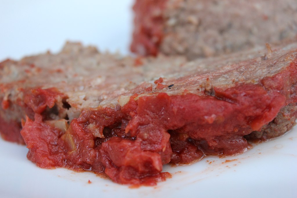 Meatloaf created with cracker crumbs, onion, ground beef, and tomato based sauce