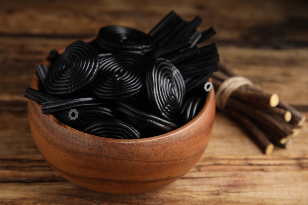 Tasty black candies and dried sticks of liquorice root on wooden table