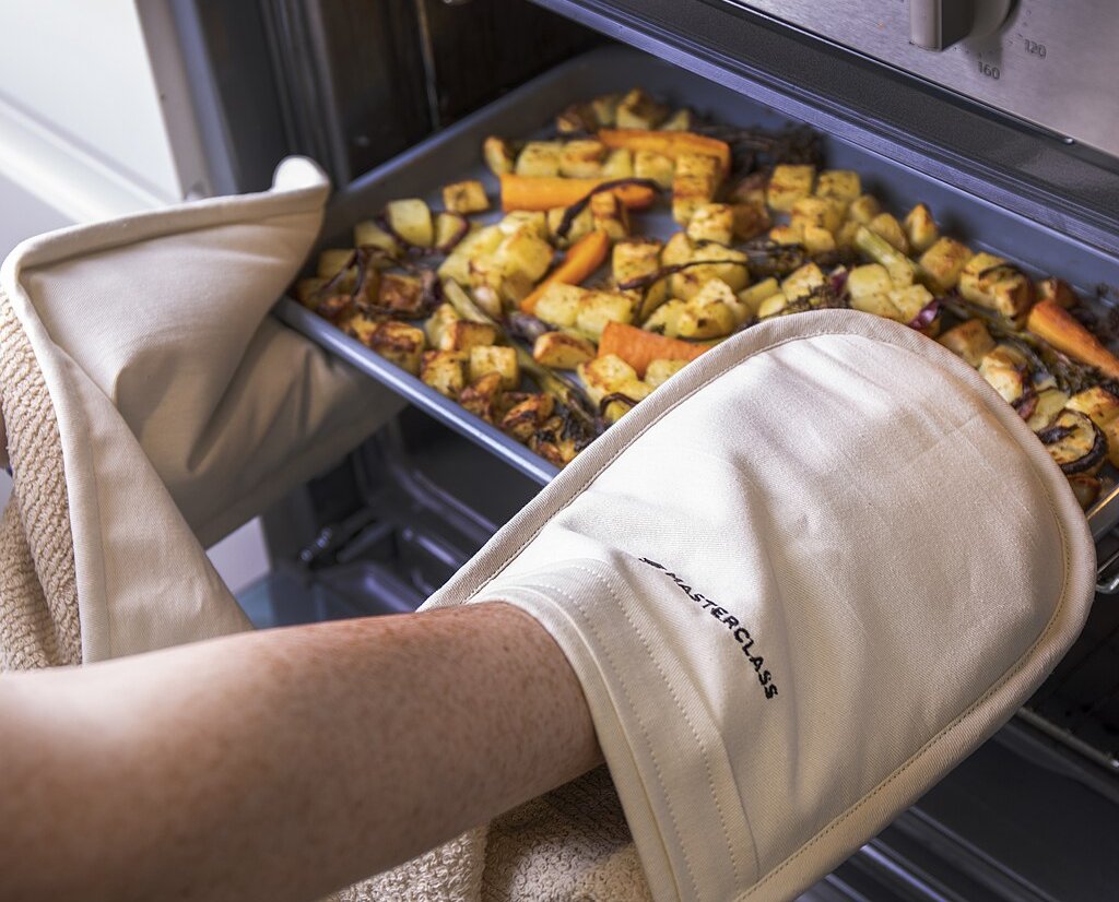 Close Up Photo of Oven mitts holding tray of roast vegetables and potatoes
