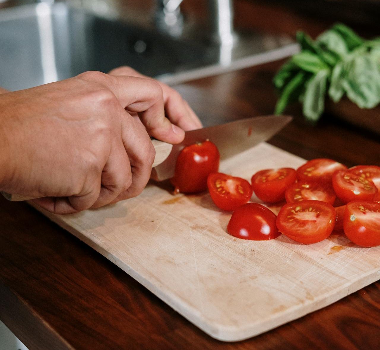 Close-up Photo Of Person Slicing cherry Tomatoes on a wooden board