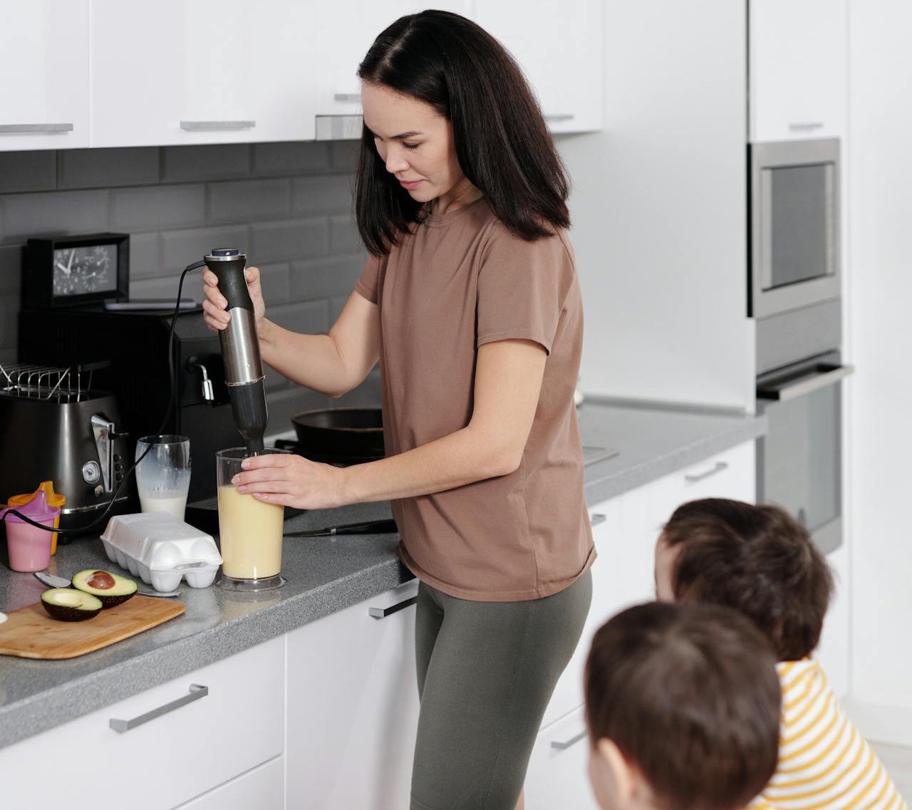 Woman Preparing Food for Children in a Kitchen using a immersion blender.
