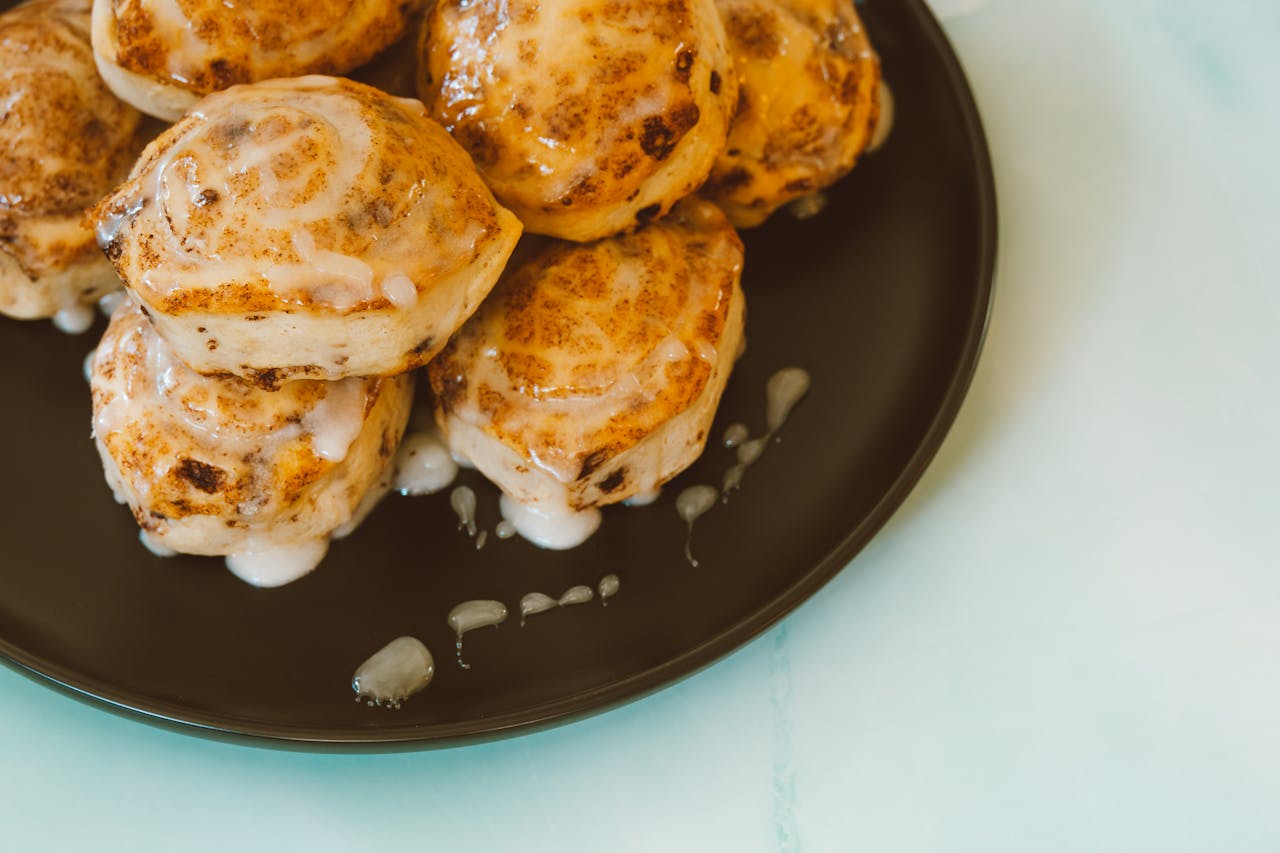 Close Up Photo of Cinnamon Rolls with Icing placed on a black plate.