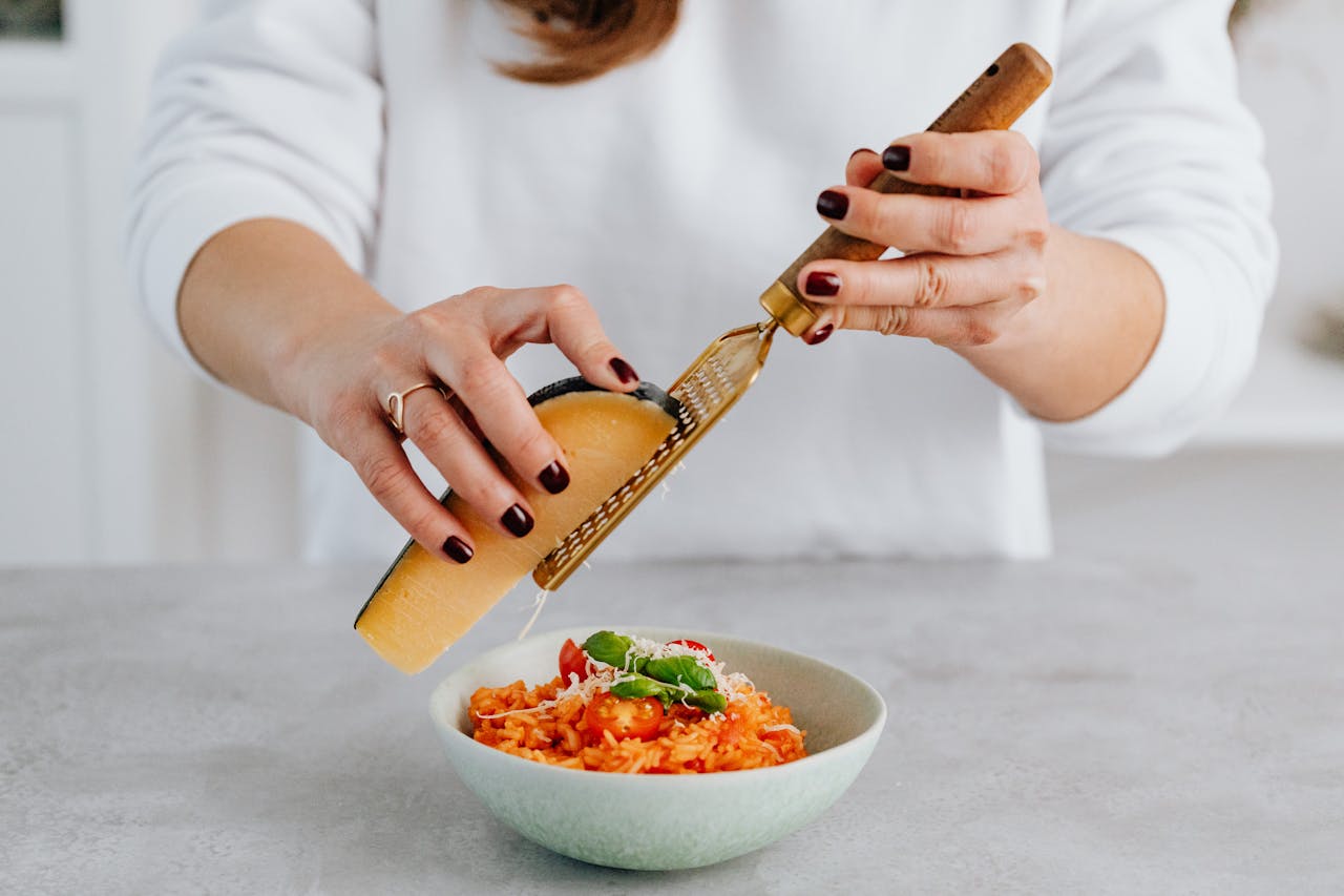 Photo of a Woman Grating Cheese on Top of a Risotto.