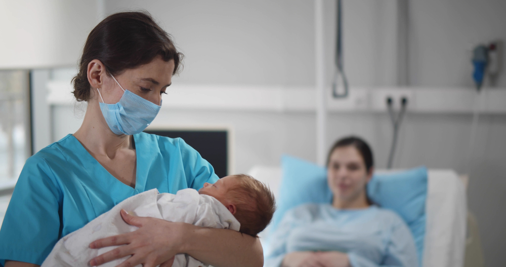 Portrait of nurse wearing safety mask cradling newborn in arms