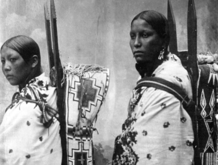 Photograph of two Kiowa women wearing wooden cradleboards