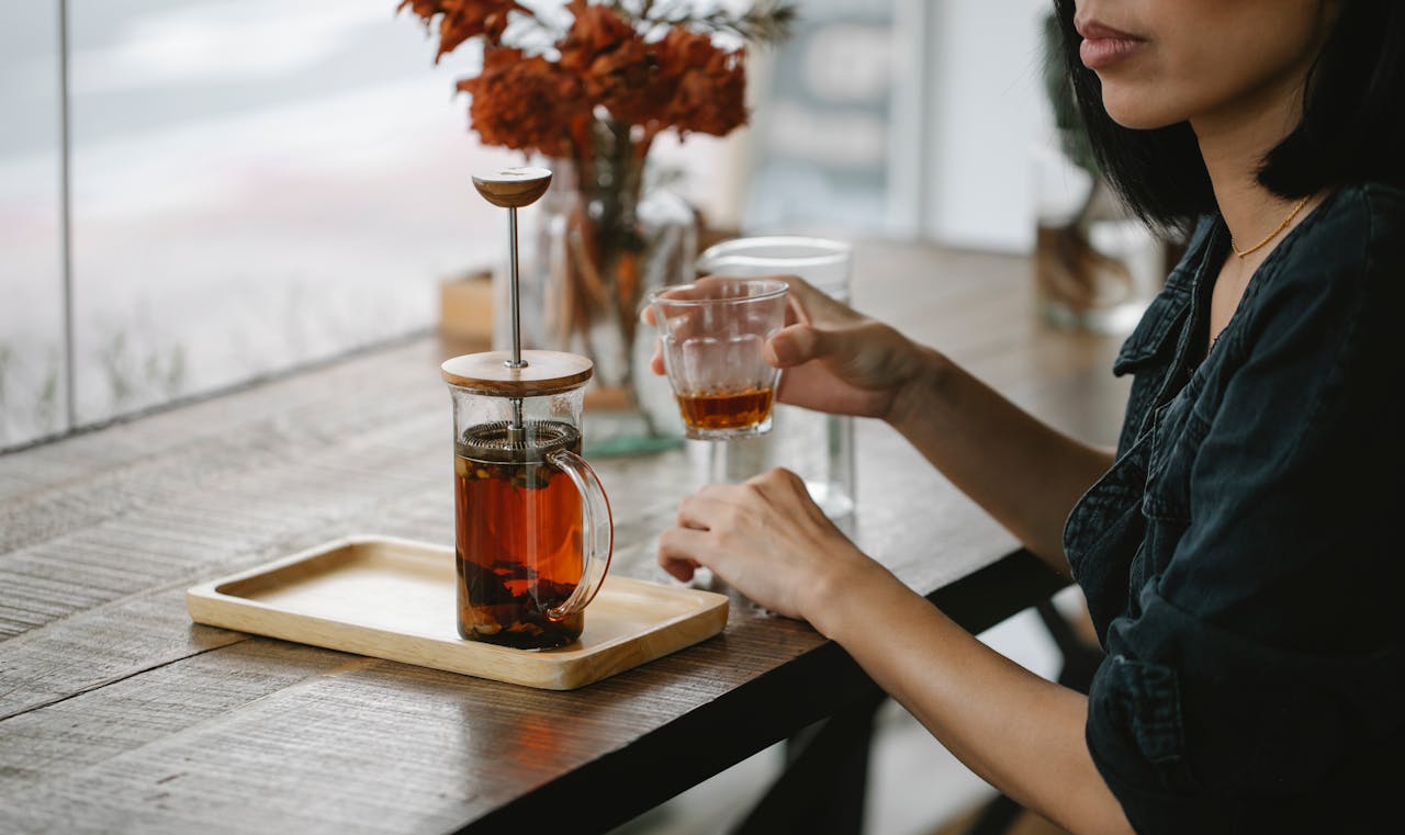 Crop woman enjoying herbal tea at high table