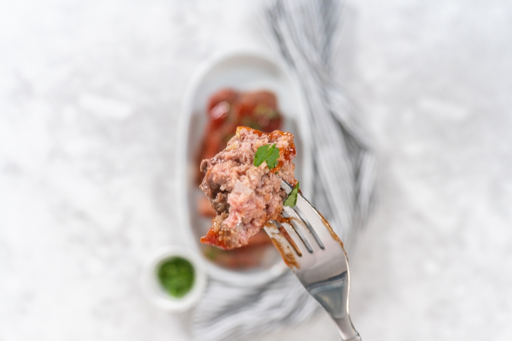 Slicing classic meatloaf with a sweet glaze on a white serving plate