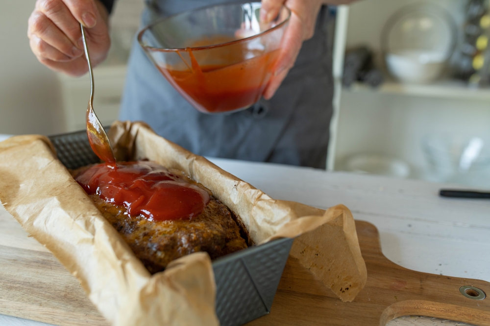 Glazing a fresh meatloaf by woman´s hands in the kitchen