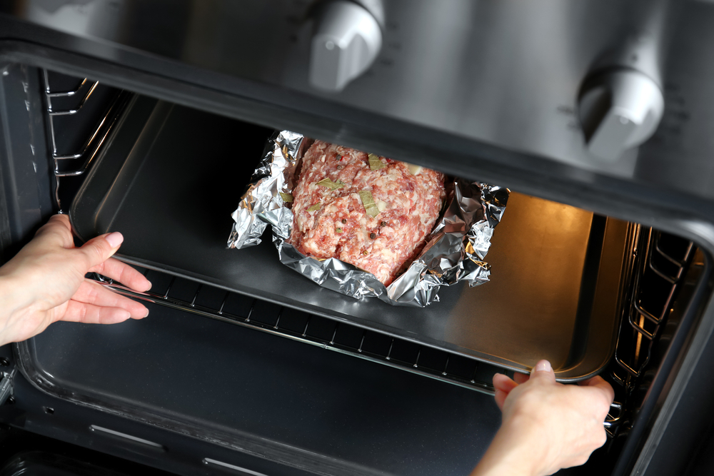 Woman putting baking tray with raw turkey meatloaf into oven.