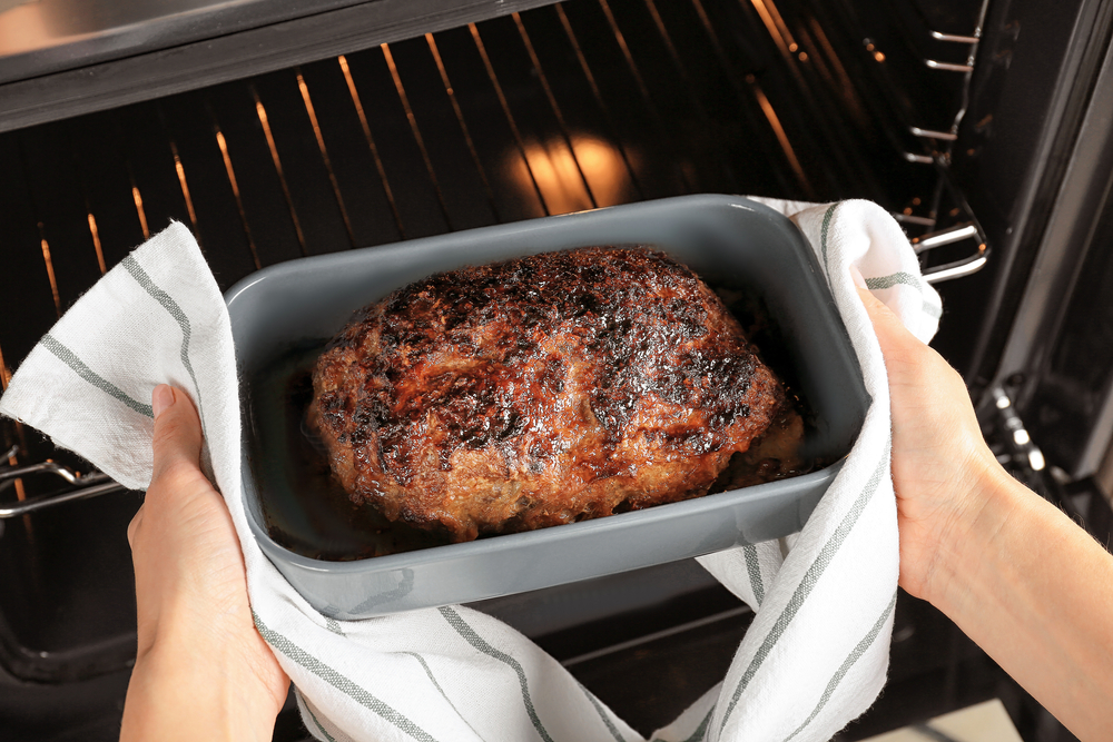 Woman taking out baked meatloaf from oven, closeup