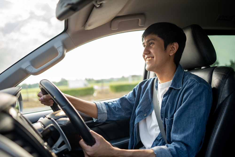 A young Asian man drives a car on a clear day.