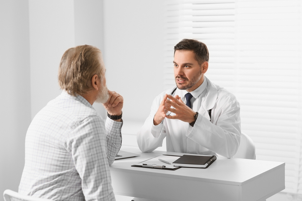 Doctor consulting senior patient at white table in clinic