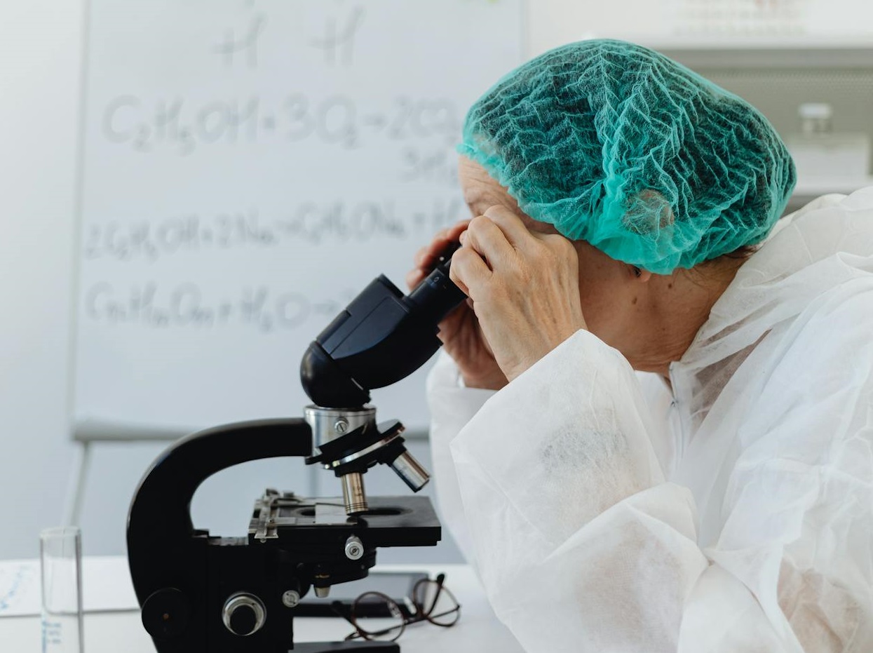 Person in White Scrub Suit Looking at the Microscope