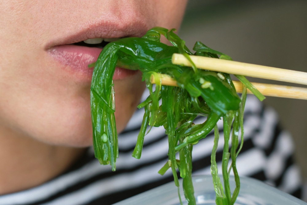 Mouth and hand of a person eating seaweed salad with chopsticks.