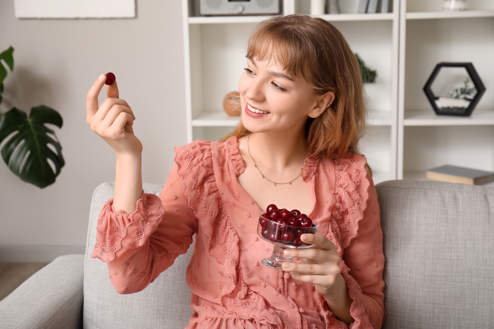 Woman with bowl full of ripe cherries sitting on sofa in living room