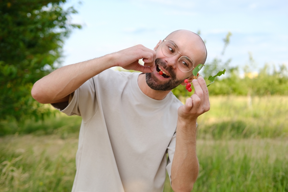 Bold man eating cherries outside.