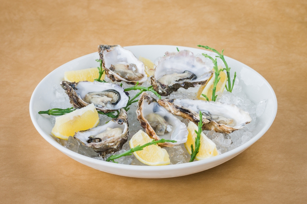 White bowl of fresh raw oysters on ice with lemon